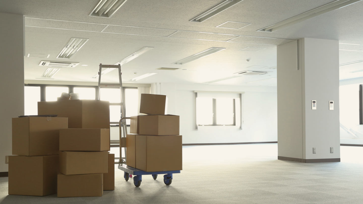 Stacked cardboard boxes and a ladder in a bright, empty office space, suggesting a move or renovation.