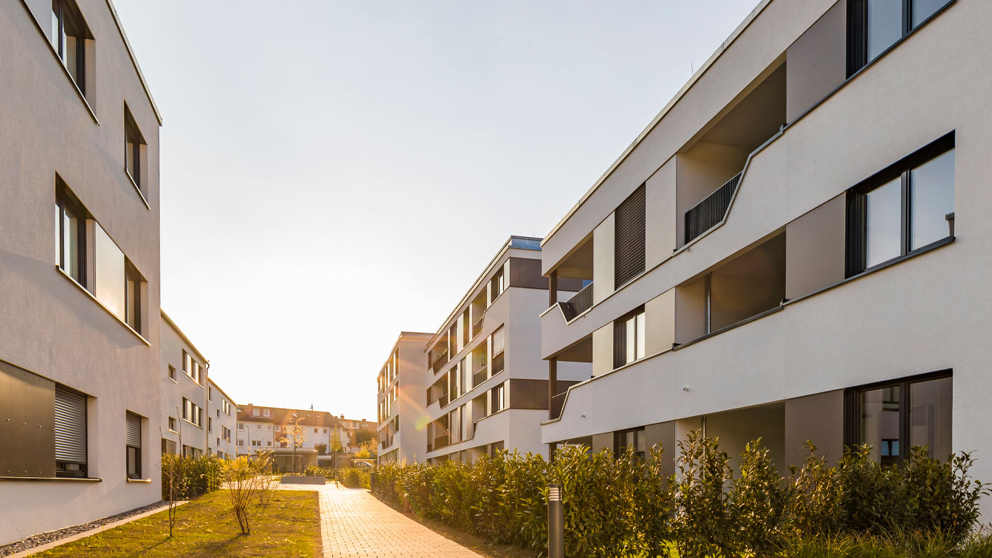 Modern apartment buildings with balconies lining a landscaped walkway, illuminated by warm sunlight.