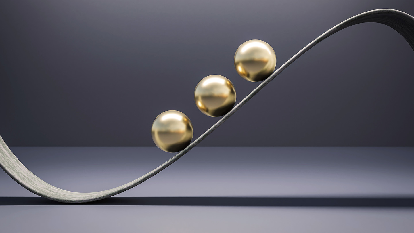 Three golden spheres balanced on a curved metallic track against a neutral background.