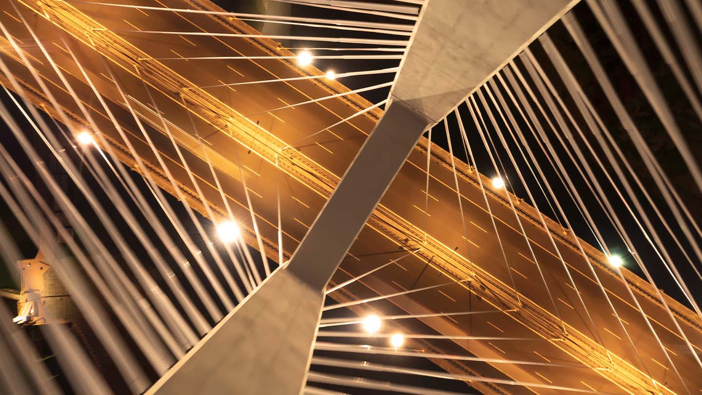 Upward view of a cable‑stayed bridge with illuminated cables and roadway at night.