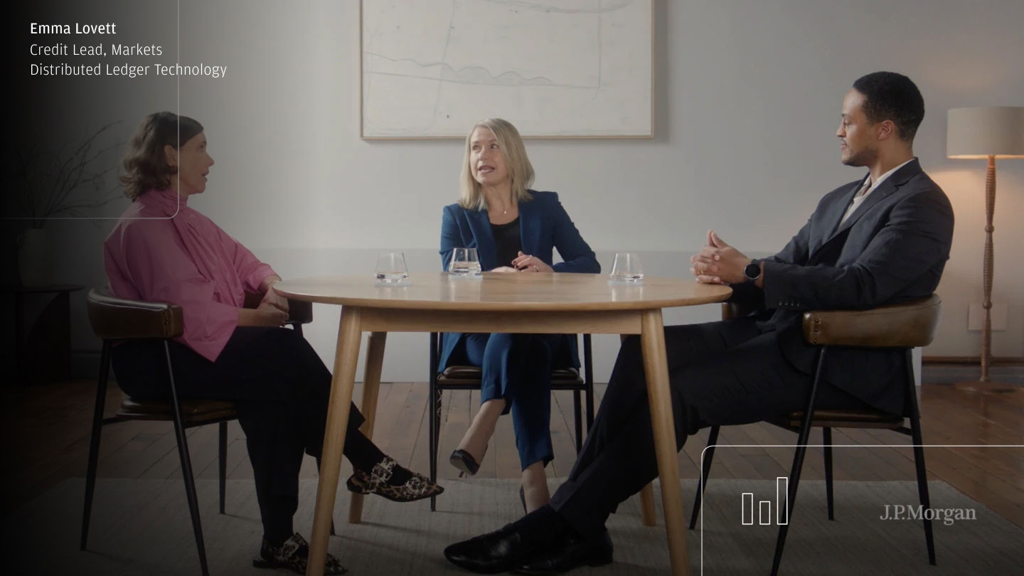 Three people in business attire sit around a table in a meeting room, with a name/title caption on screen and a “J.P. Morgan” watermark.