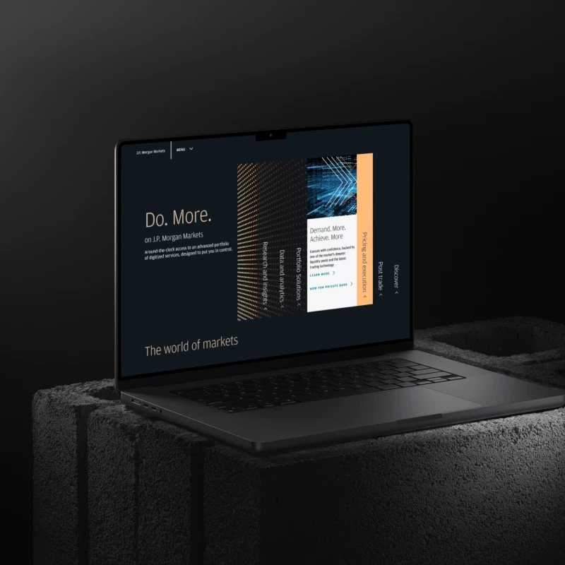 Laptop on a dark textured surface displaying a J.P. Morgan Markets webpage with the headline “Do. More.” and a visual panel of market-content tiles, set against a moody black background.
